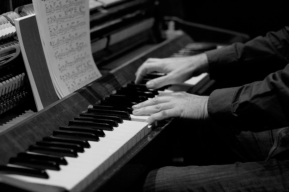 Pianist playing while reading from sheet music placed on a music stand, showing hands on keys and the music.