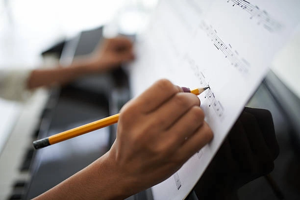Close-up of writing musical notes with a pen in a notebook on a music stand.